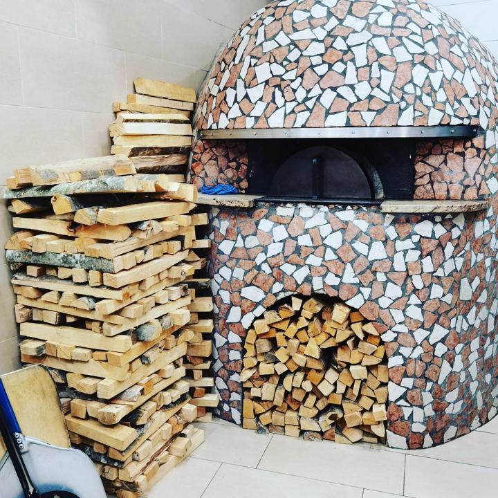 Legna mista accatastata accanto a un forno da pizza